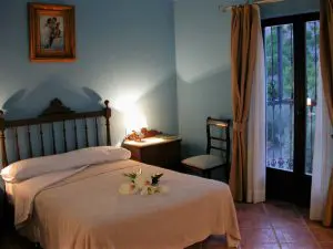 Habitación con paredes azules, y cama antigua con cabecero de varales de madera. Sobre la cama, el cuadro del Primo Baccio (el primer beso) del artista italiano Raphaelo.