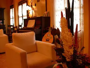 Detalle del sillón del salón principal, al fondo piano con flores encima.